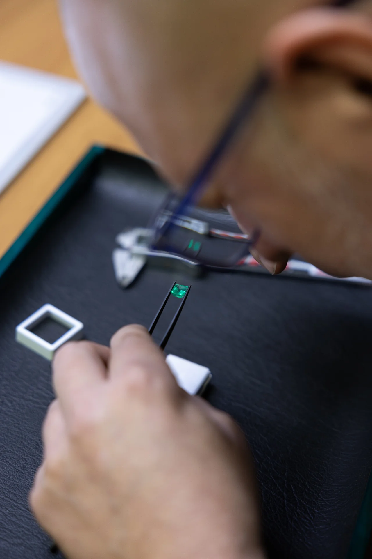 Gemmologo mentre esamina uno smeraldo con pinzette e lente di ingrandimento in laboratorio di gioielleria